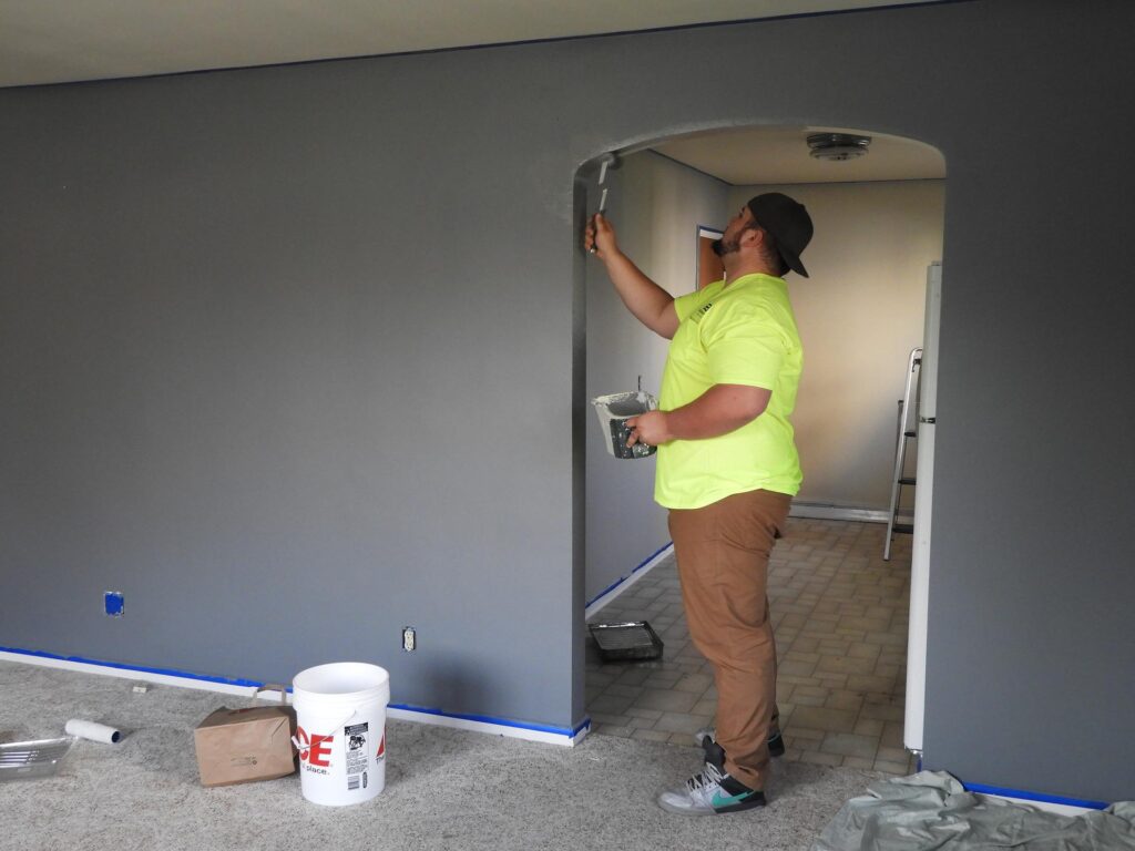 mężczyzna remontujący mieszkanie maluje wnękę drzwi i ścianę na szaro